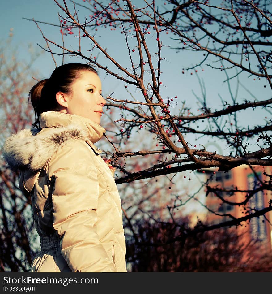 Girl in beige dawn parka and red berry tree on the background. Girl in beige dawn parka and red berry tree on the background