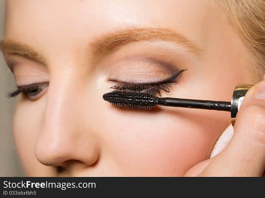 Charming young woman applying blusher eyelid. Close-up view.