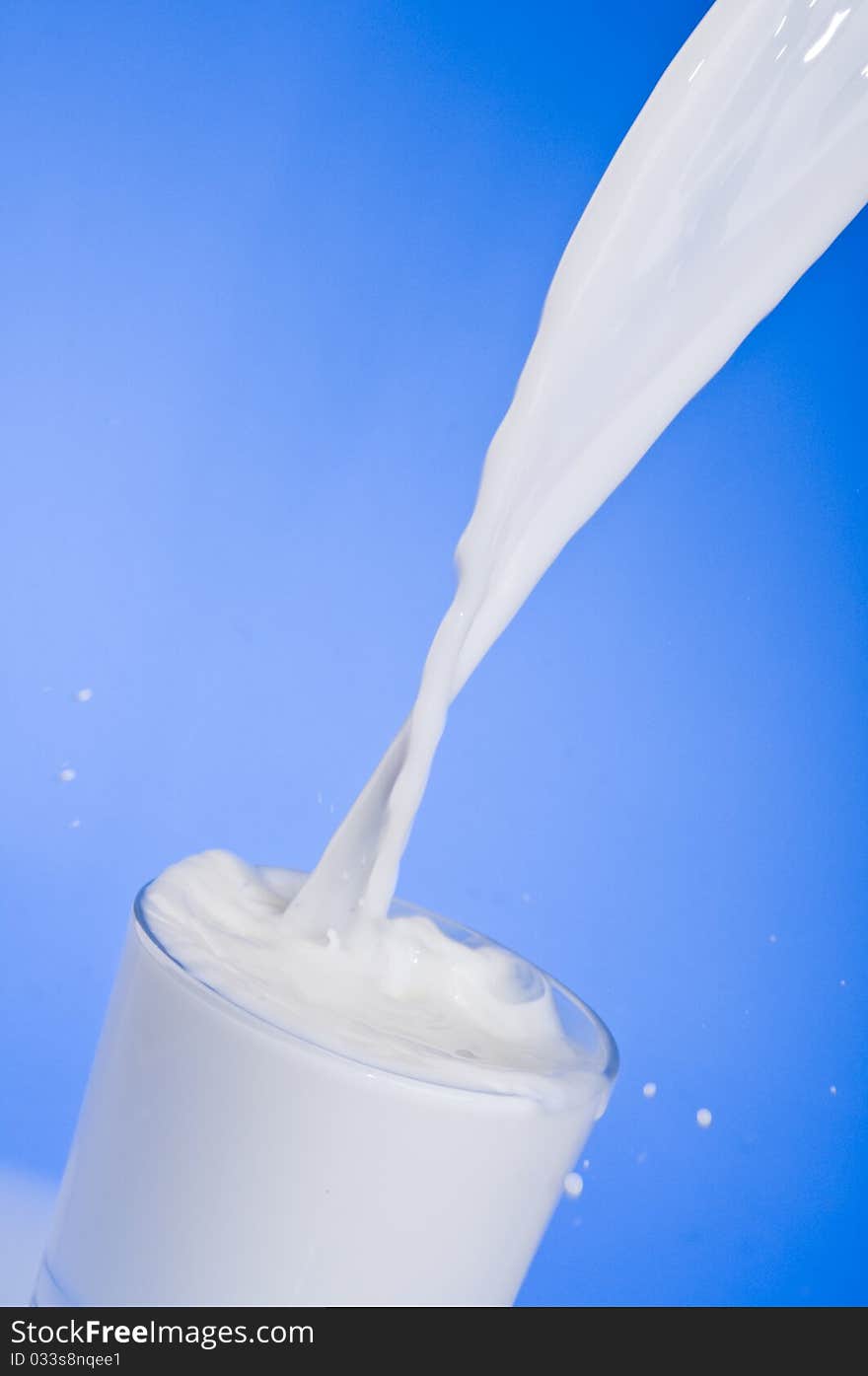 Pouring milk into a glass isolated over blue background