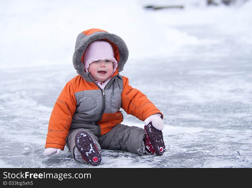 Cute wondered baby sit on lake's ice and smile holding boot