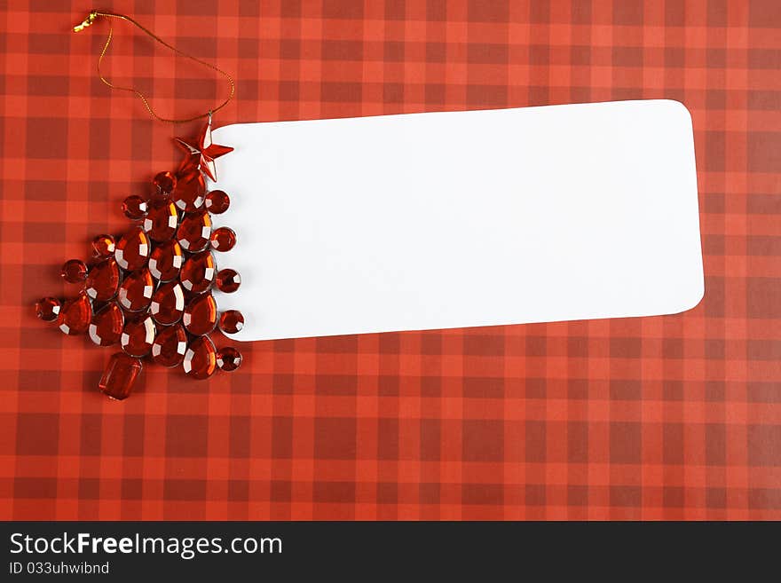 Christmas card with a red decorations in the form of a Christmas tree made of precious stones next to a white sheet of paper