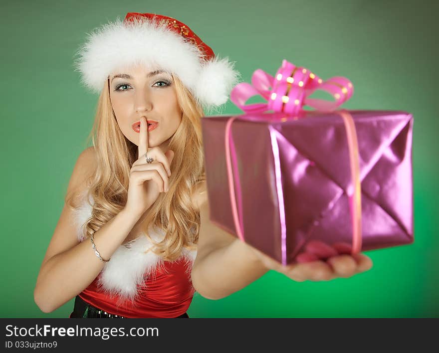 Woman wearing Santa clothes and holding a gift on a green background. Woman wearing Santa clothes and holding a gift on a green background