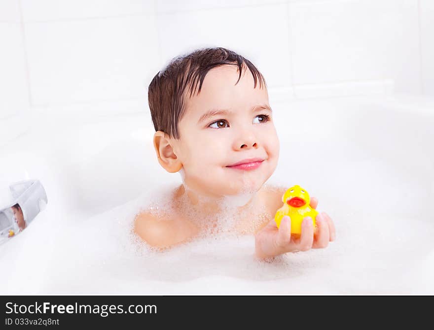 Cute four year old boy taking a relaxing bath with foam and playing with a toy duck. Cute four year old boy taking a relaxing bath with foam and playing with a toy duck