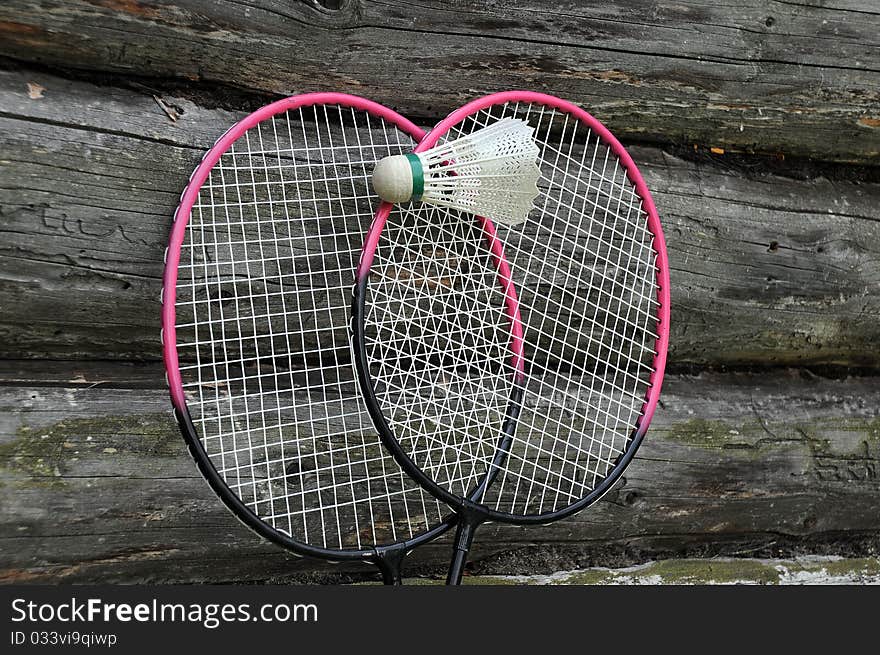 Two badminton rackets and a ball on the wall of the wooden house. Two badminton rackets and a ball on the wall of the wooden house