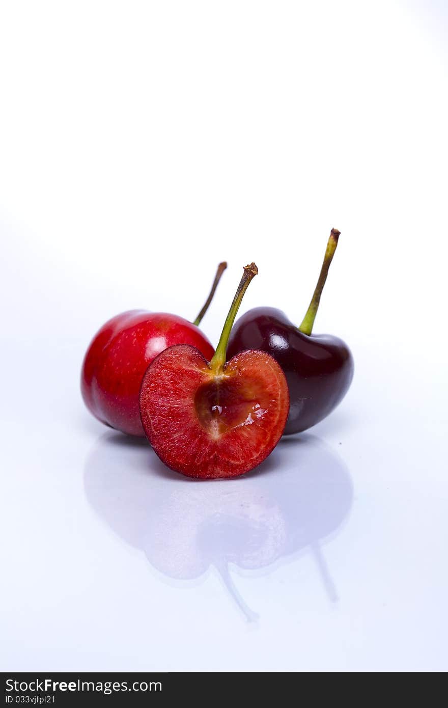 One cut fresh cherry against two whole fresh cherries isolated on white background with reflection in foreground. One cut fresh cherry against two whole fresh cherries isolated on white background with reflection in foreground.