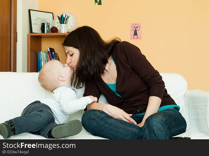 Young mother kissing her small child on a sofa. Young mother kissing her small child on a sofa