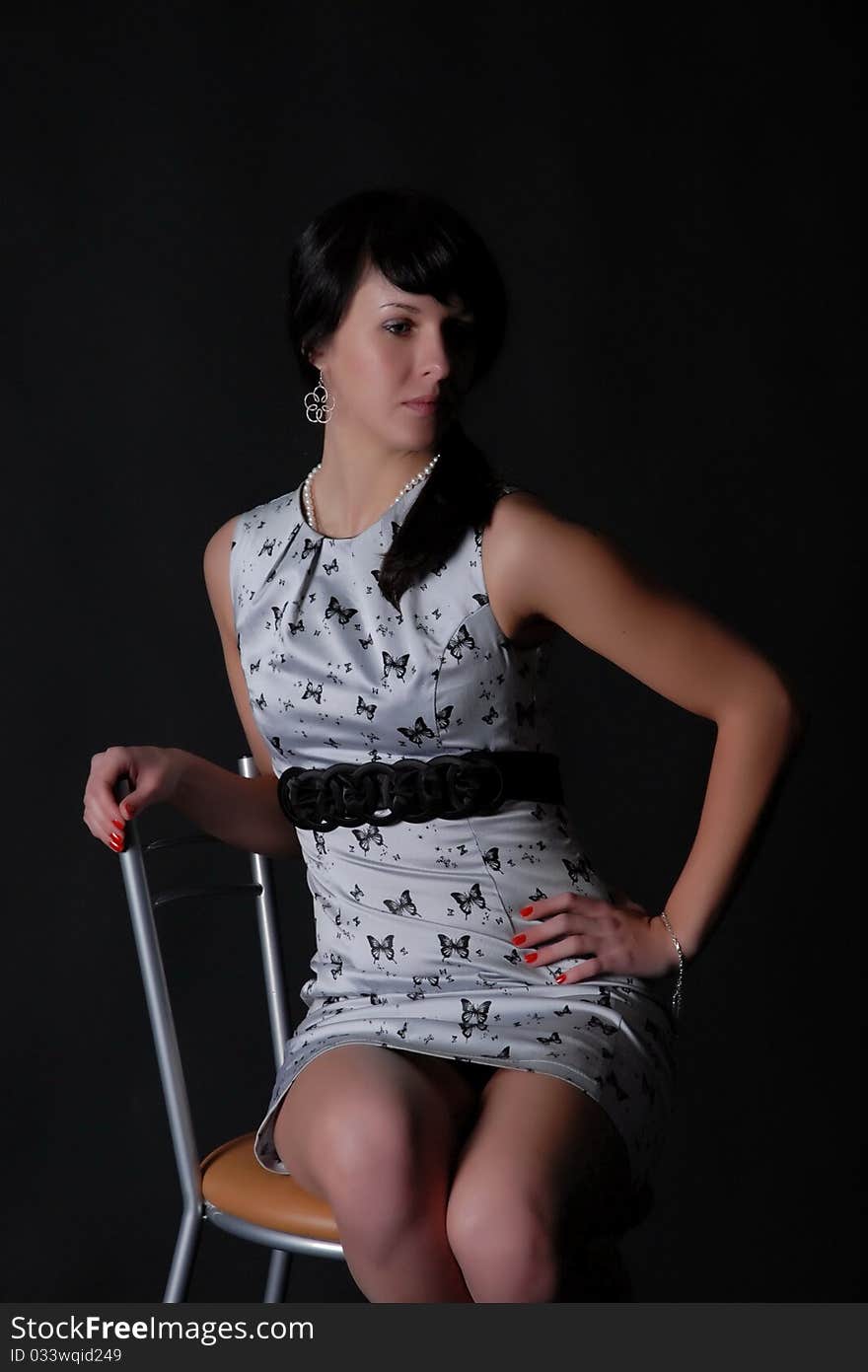 Thoughtful brunette on a chair on a dark background. Thoughtful brunette on a chair on a dark background