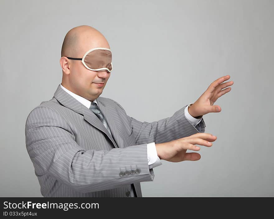 Bald businessman in a gray suit with a gray background with a bandage to sleep in his eyes