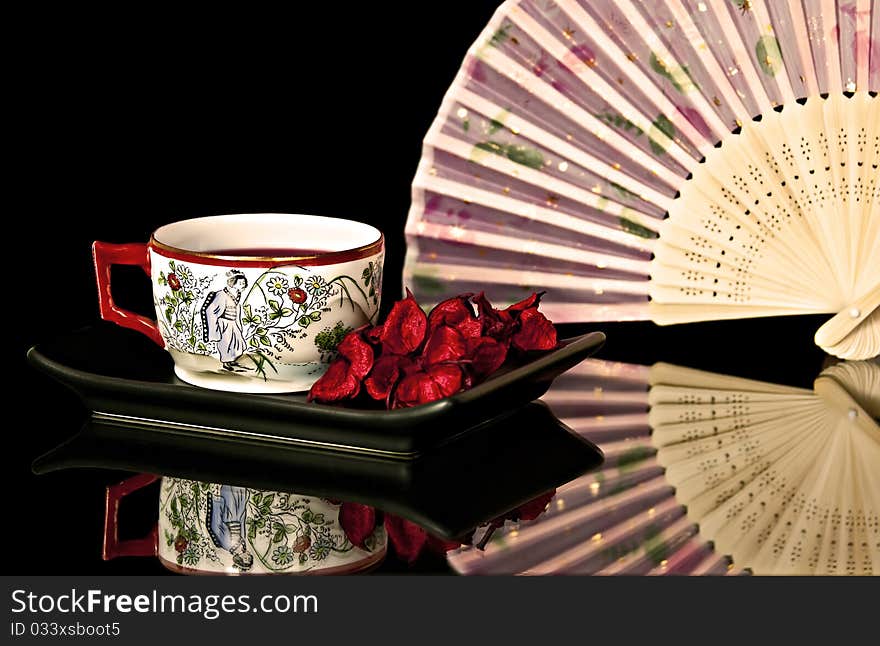 An antique teacup with a design. Rear trunnions fan in the background. An antique teacup with a design. Rear trunnions fan in the background.