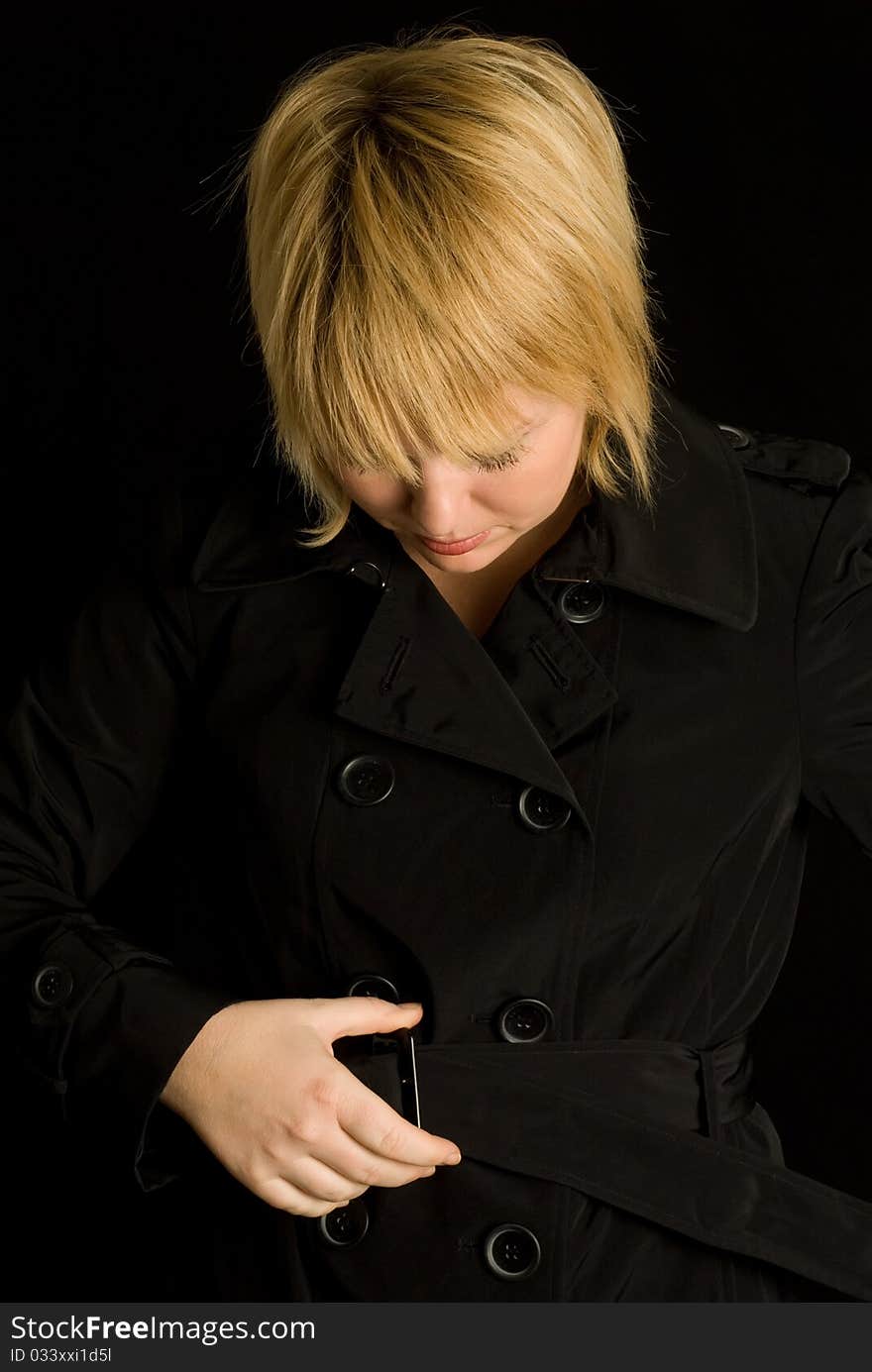 Blond woman fastening belt on black trench coat. Blond woman fastening belt on black trench coat.