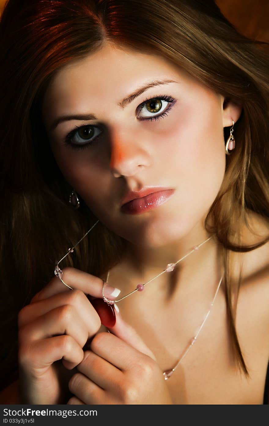 Beautiful young woman with hands on necklace over dark background. Beautiful young woman with hands on necklace over dark background.