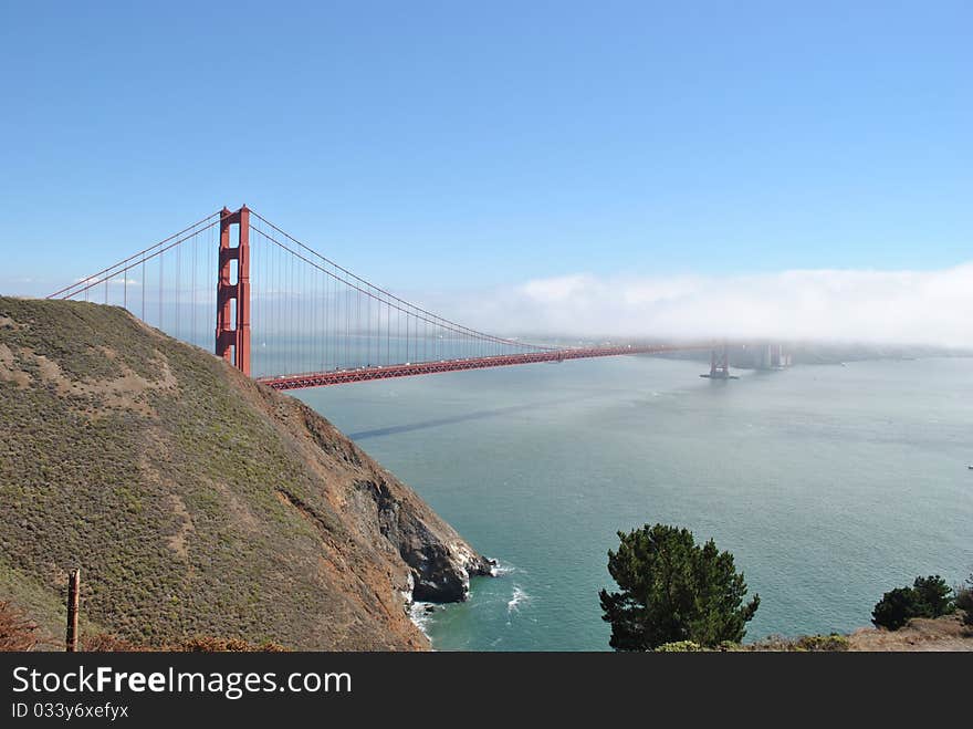 View of the Golden Gate Bridge, on a bright summer day. A layer of fog had just rolled in off the ocean, masking part of the bridge and hiding the city from view in the background. View of the Golden Gate Bridge, on a bright summer day. A layer of fog had just rolled in off the ocean, masking part of the bridge and hiding the city from view in the background