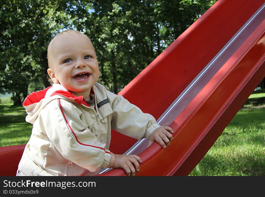 Happy baby on the red slide in a park. Happy baby on the red slide in a park