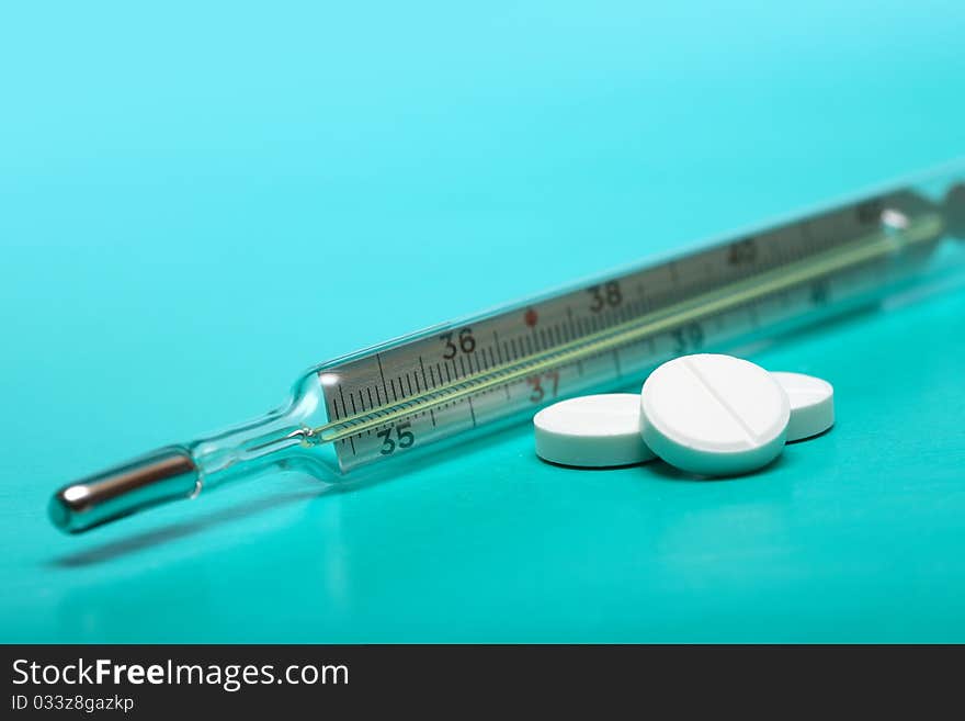 Stack of pills near clinical thermometer on green background. Stack of pills near clinical thermometer on green background