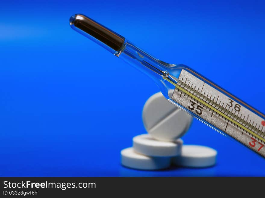 Clinical Thermometer closeup on blue background with stack of pills. Clinical Thermometer closeup on blue background with stack of pills