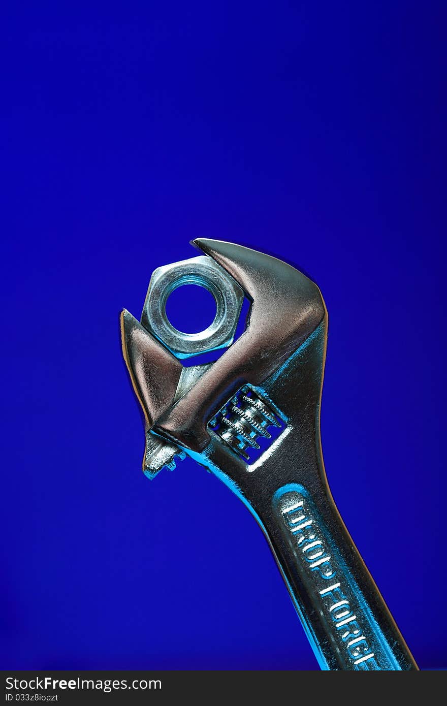 Extreme closeup of adjustable wrench gripping a nut on blue background. Extreme closeup of adjustable wrench gripping a nut on blue background