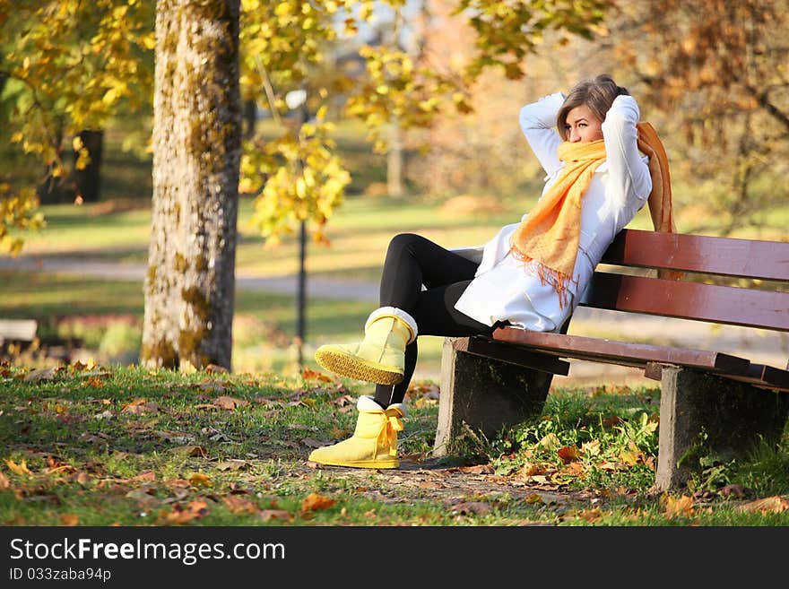 Young woman sitting on bench in park and tying her scarf