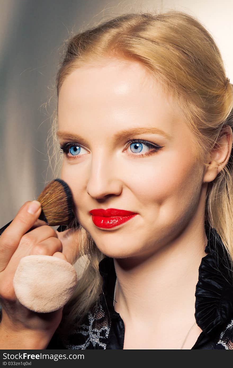 Close-up portrait of charming young woman applying blusher eyelid