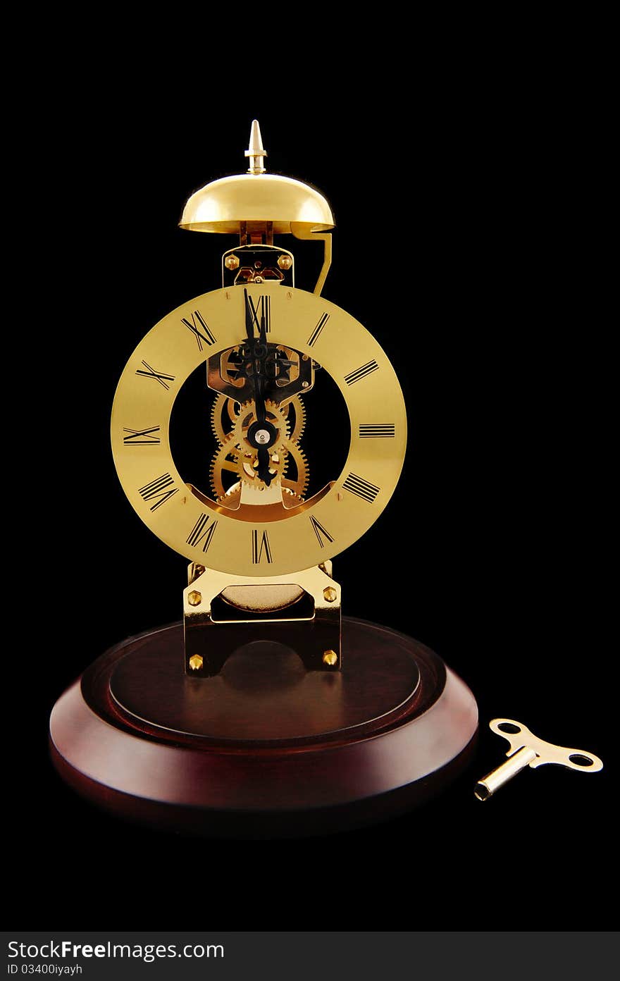 An old-fashioned, gold colored, windup clock with its key.  Isolated on black. An old-fashioned, gold colored, windup clock with its key.  Isolated on black.