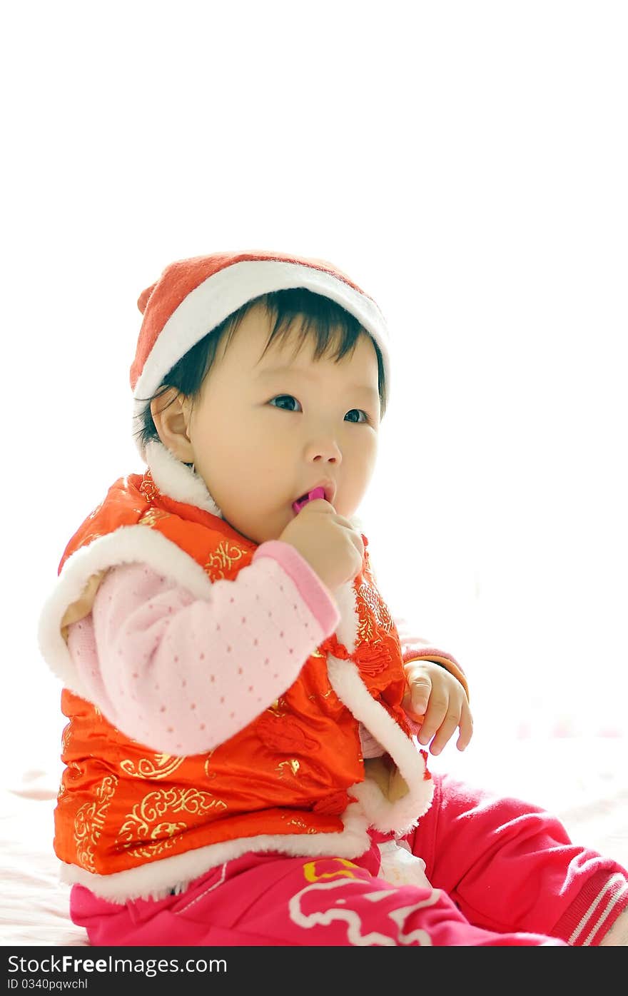 A Asian baby girl sitting on the bed，who Wearing a Christmas hat