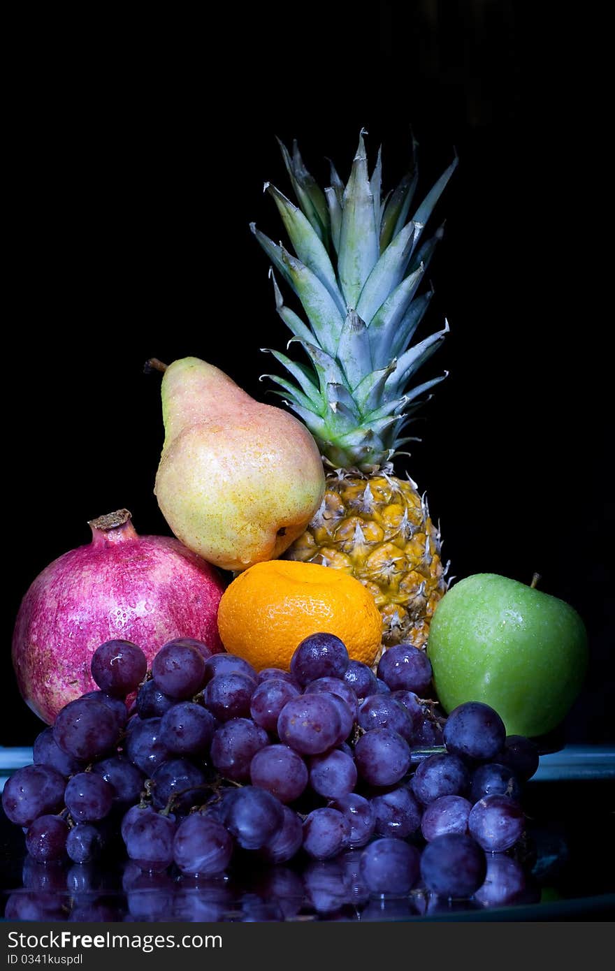 Fruit: pineapple, grapes, a tangerine, a pomegranate, a green apple against a dark background. Fruit: pineapple, grapes, a tangerine, a pomegranate, a green apple against a dark background