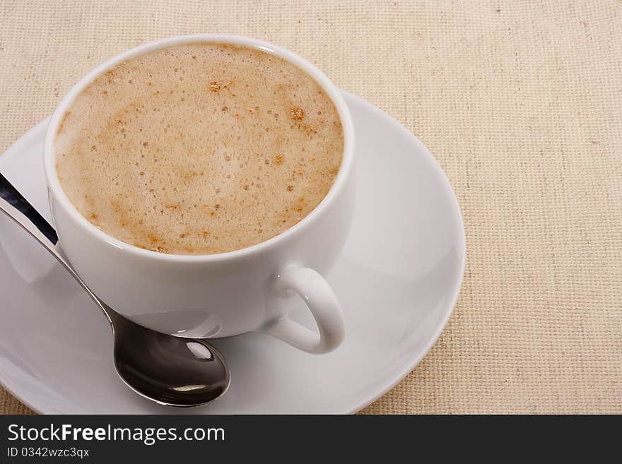 Cappuccino in a white ceramic cup with a saucer and a spoon.