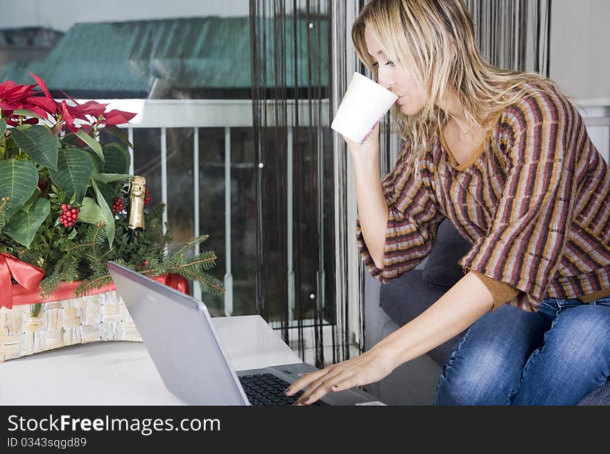 Happy blond woman on her couch working on her laptop and taking a sip from her coffee. Happy blond woman on her couch working on her laptop and taking a sip from her coffee