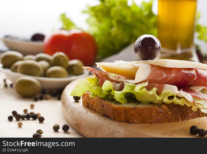 Prosciutto and cheese sandwich with olives and lettuce.Focus is on the cheese. Shallow depth of field.