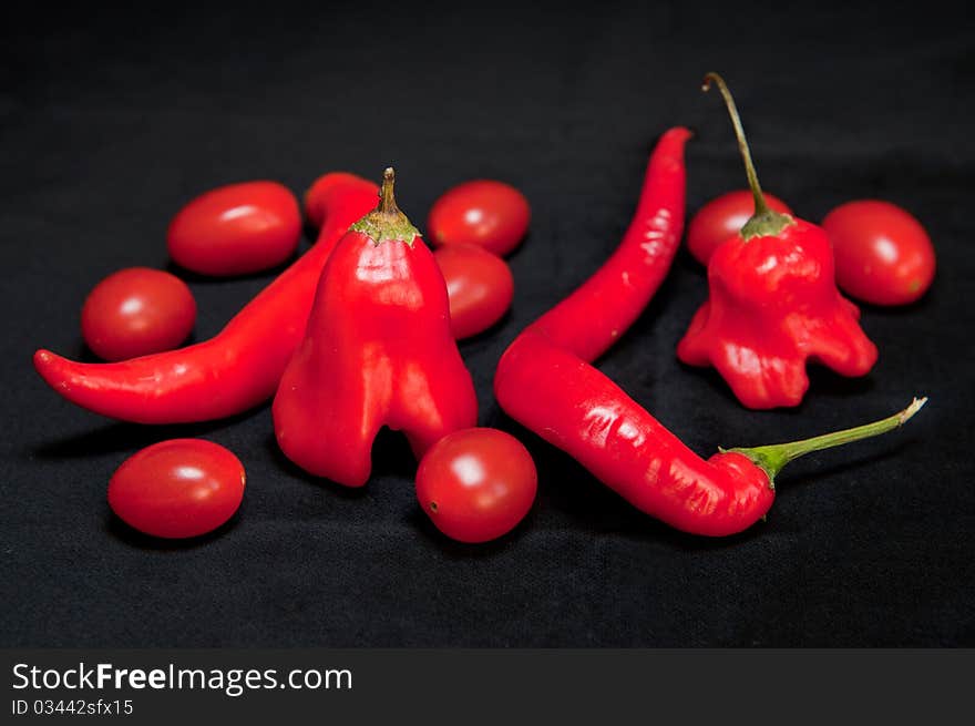 Red hot chilli peppers and cherry tomatoes isolated on a black background.