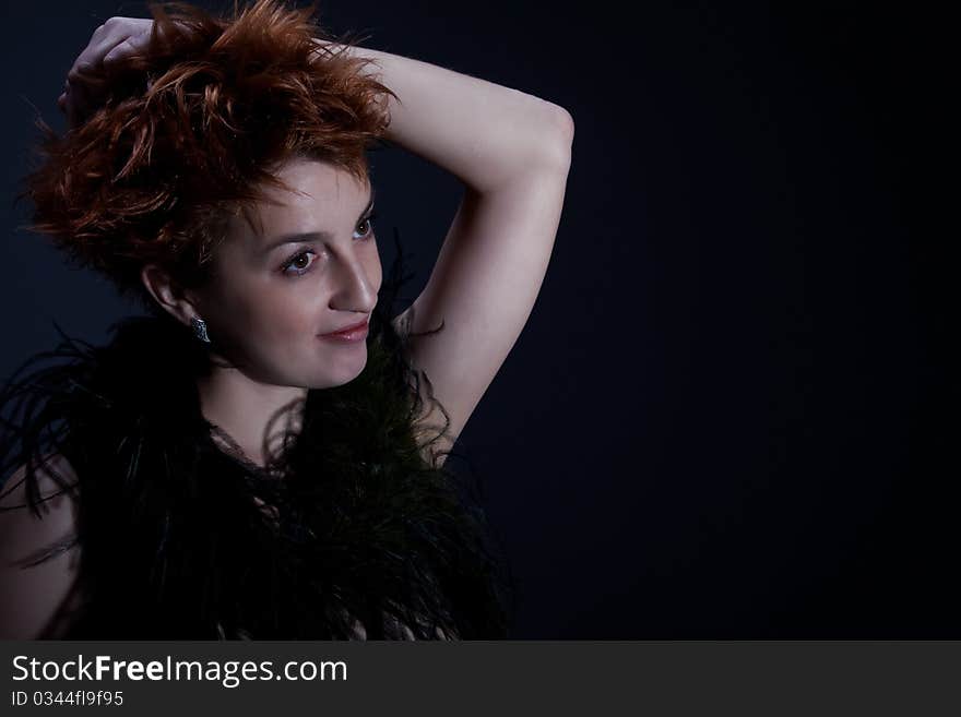 Portrait the red girl against a dark background dressed in a boa