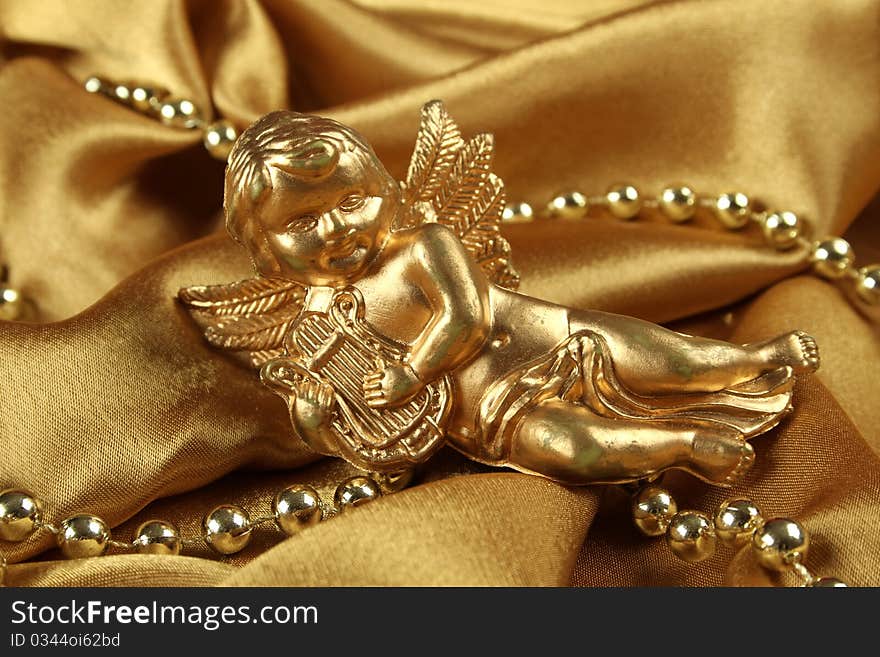 Little gold angel with a harp lying on the golden cloth beside ornaments. Background. Little gold angel with a harp lying on the golden cloth beside ornaments. Background