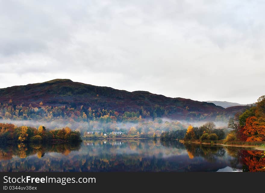 Still water on Grasmere with reflections of Autumn colours and mist. Still water on Grasmere with reflections of Autumn colours and mist