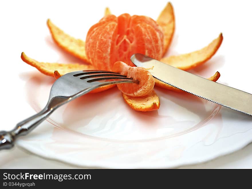 Cleared mandarine on a plate, plug, knife.