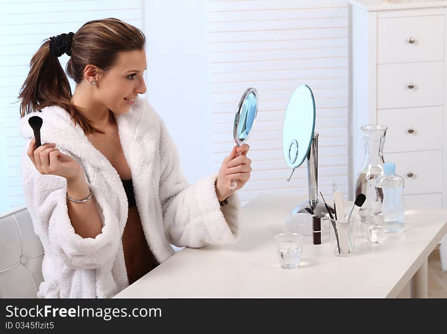 Beautiful brunette woman sitting in a bathroom and doing her make up. Beautiful brunette woman sitting in a bathroom and doing her make up