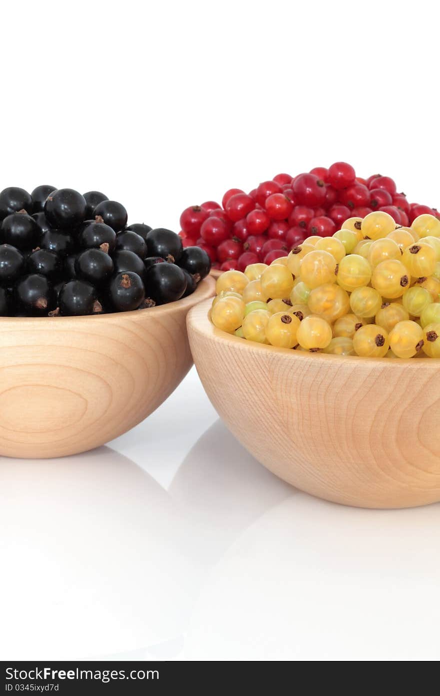 Red, black and white currants in beech wood bowls over white background.