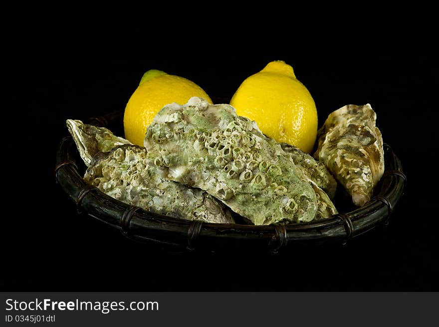 Oysters and lemons in a basket on black background