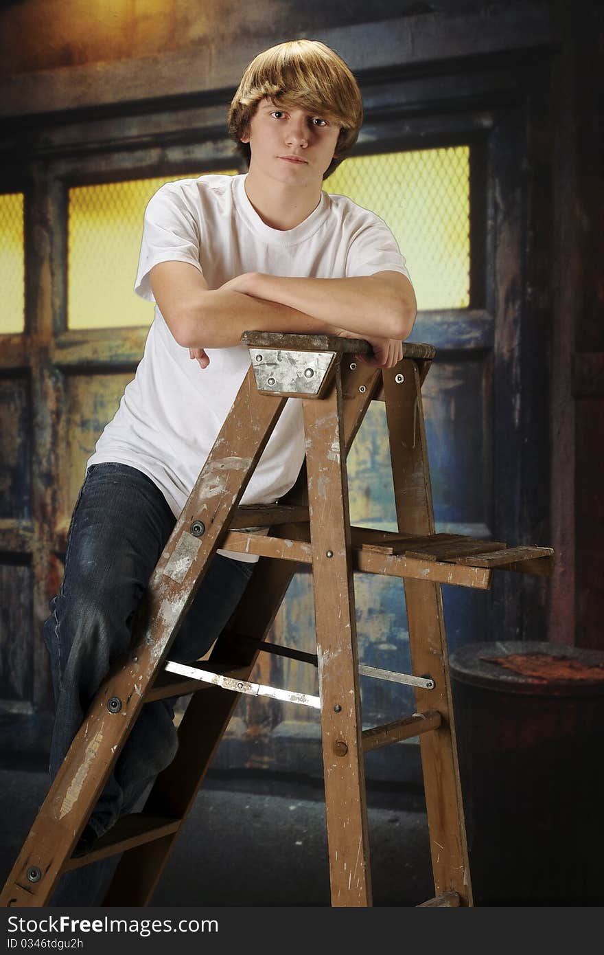 A serious young teen on a ladder inside a grungy, old garage. A serious young teen on a ladder inside a grungy, old garage.