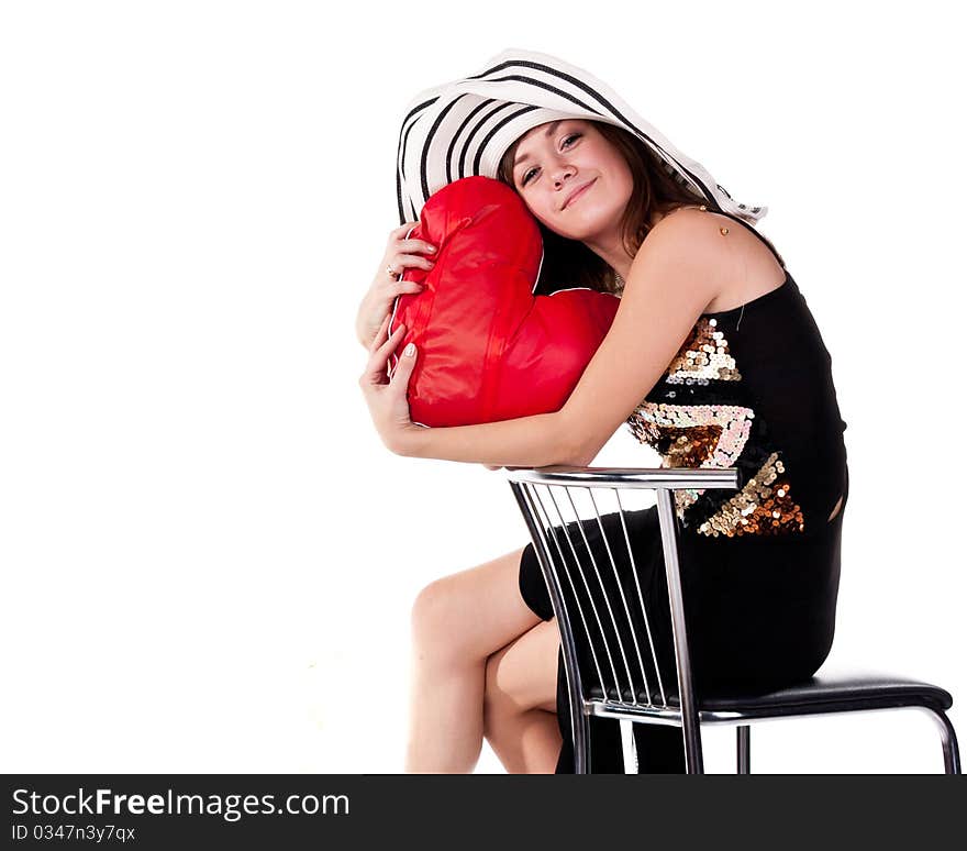 Beautiful young girl sitting on a bar chair with red heart pillow isolated on white