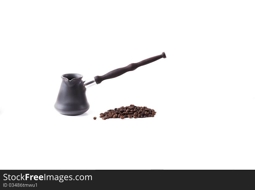 Coffee maker from dark metal with the long wooden handle of dark color and coffee grains fried on a white background. Coffee maker from dark metal with the long wooden handle of dark color and coffee grains fried on a white background