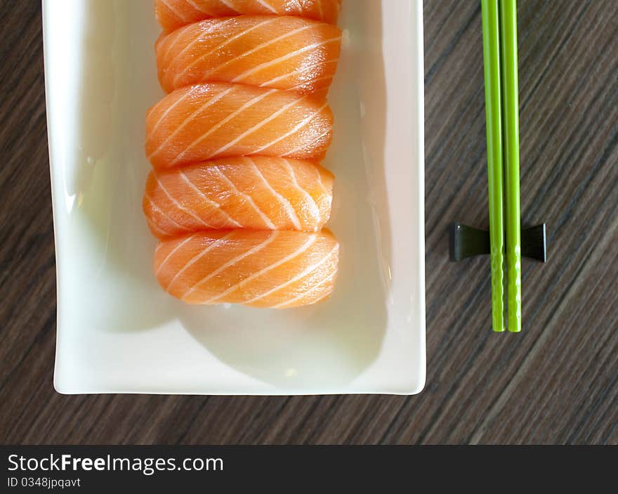 Salmon Sushi on plate with green chopsticks on wood table. Salmon Sushi on plate with green chopsticks on wood table