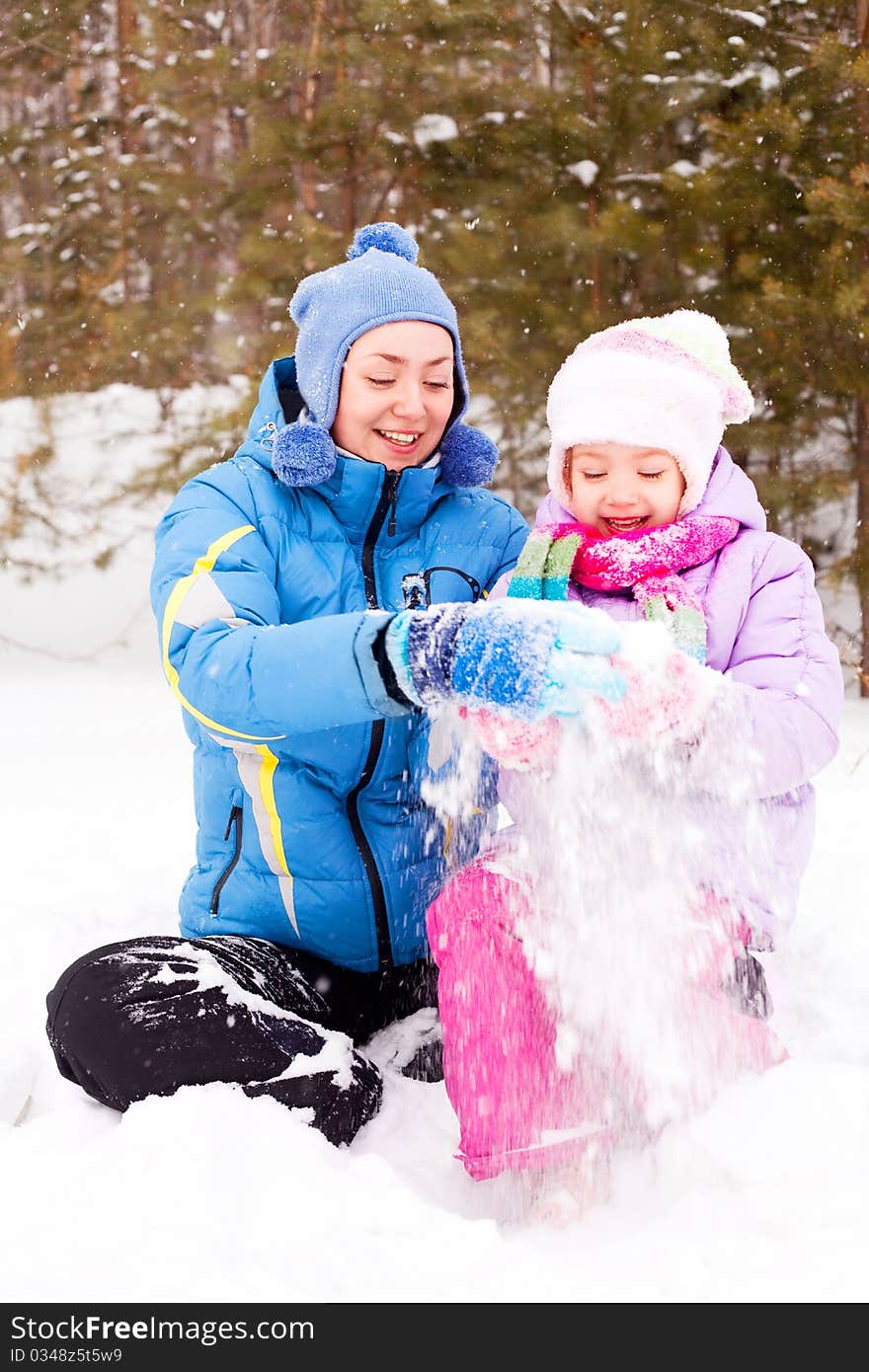 Happy family; young mother and her daughter having fun in the winter park (focus on the woman). Happy family; young mother and her daughter having fun in the winter park (focus on the woman)