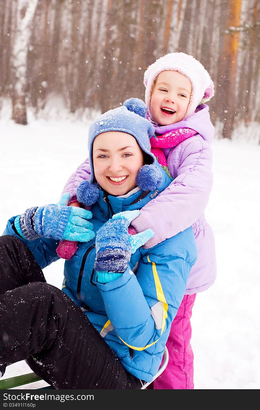 Happy family; young mother and her daughter with a sled having fun in the winter park (focus on the child). Happy family; young mother and her daughter with a sled having fun in the winter park (focus on the child)