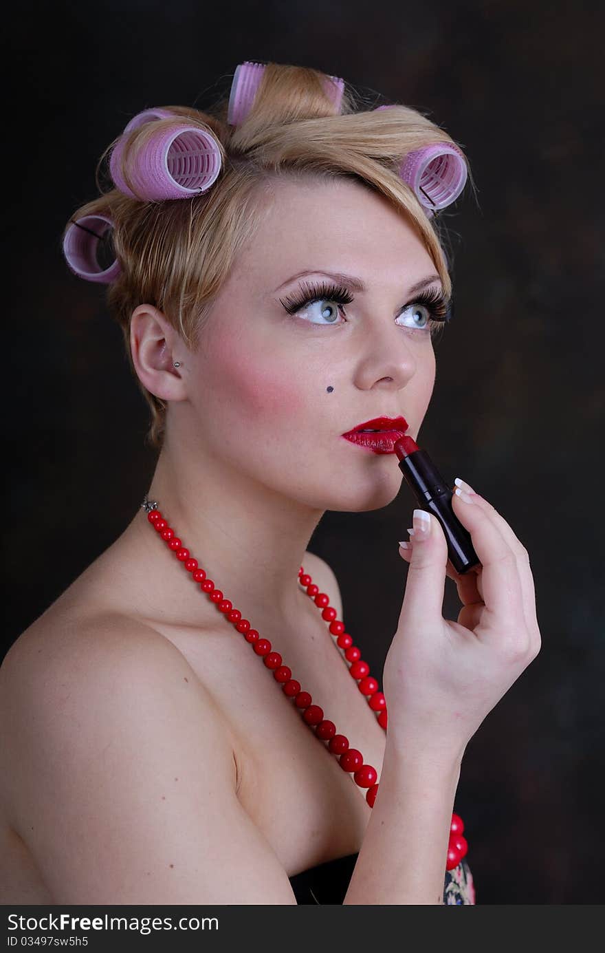 Photograph showing retro style 50s female posing against black applying lip stick. Photograph showing retro style 50s female posing against black applying lip stick