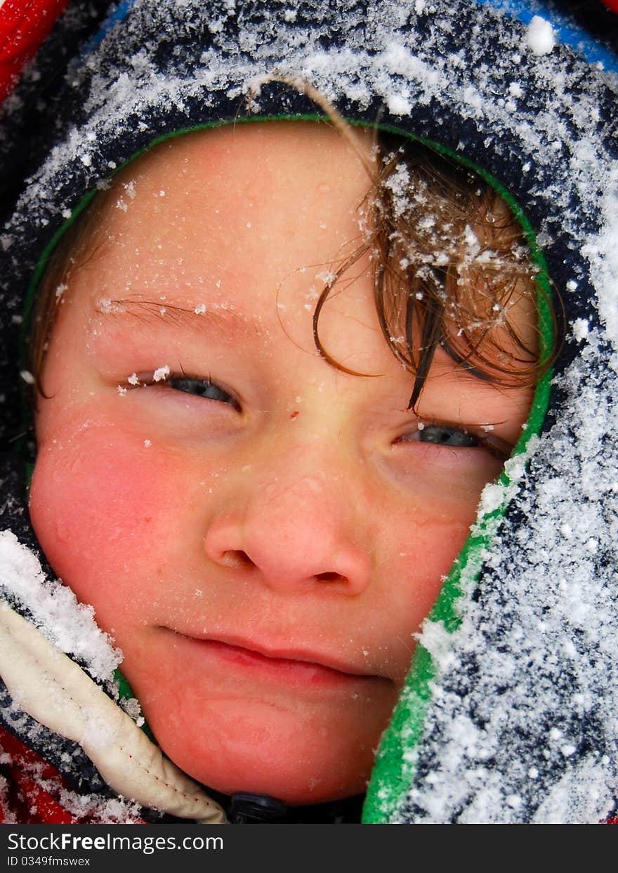 A white caucasian toddler boy of the face wearing a hat and covered with snow. A white caucasian toddler boy of the face wearing a hat and covered with snow.