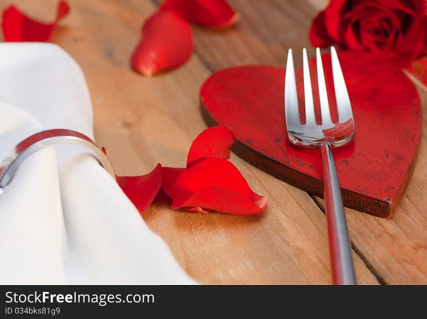 Place setting with red petals on a wooden table in country style. Place setting with red petals on a wooden table in country style