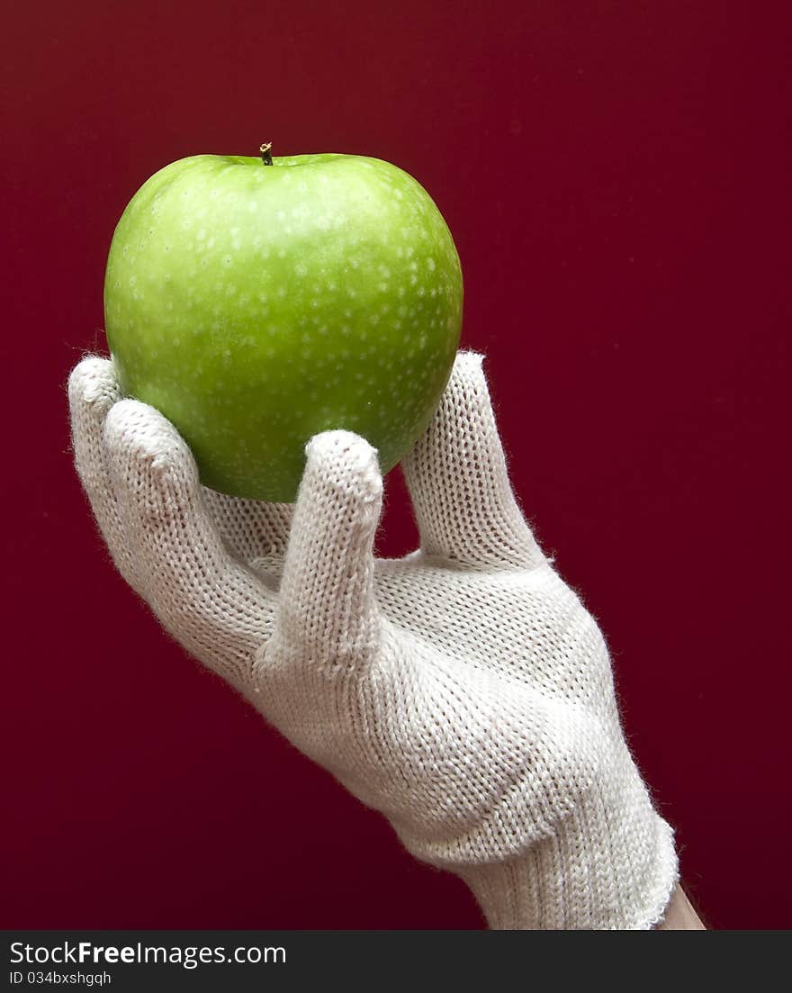 A hand in white glove holding an apple on red background