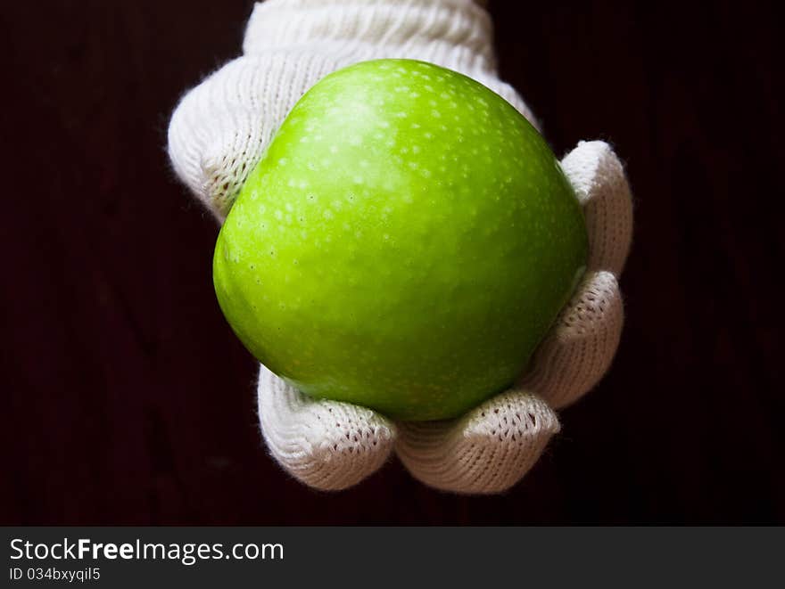 A hand in white glove holding an apple on dark background