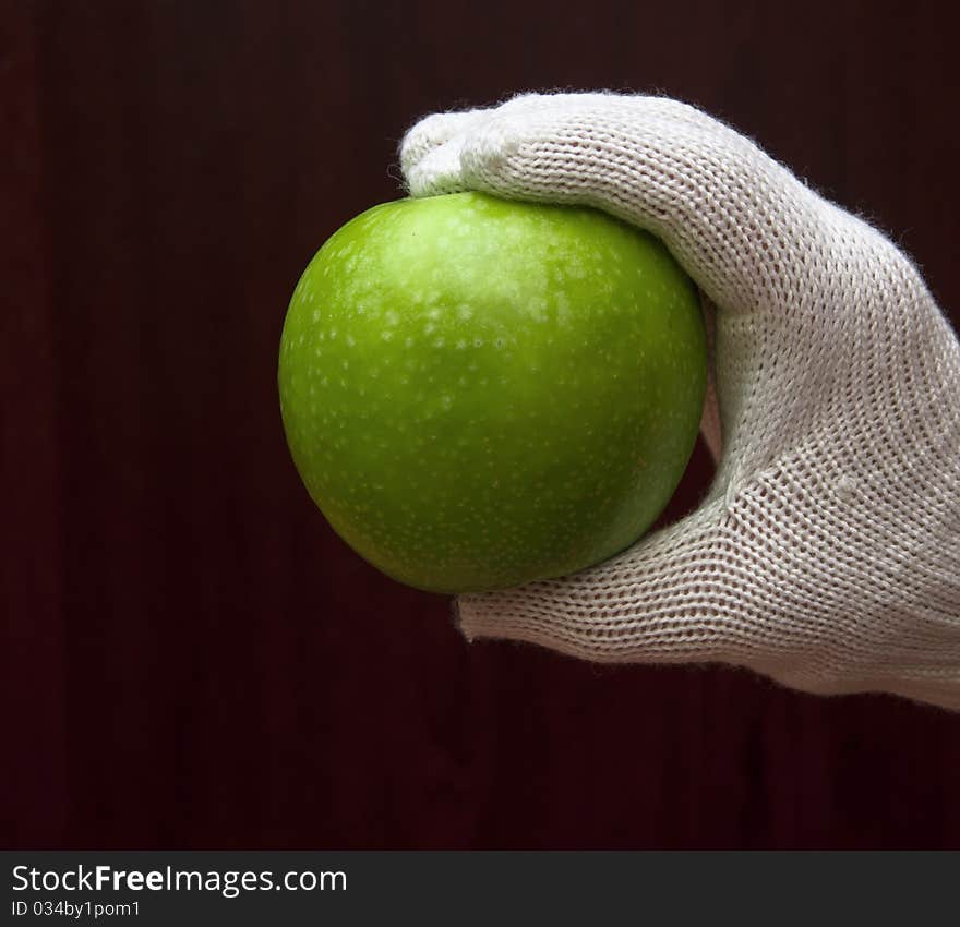 A hand in white glove holding an apple on dark background