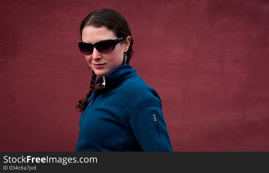 Young woman in sun glasses with braids in blue sweater on red background. Young woman in sun glasses with braids in blue sweater on red background