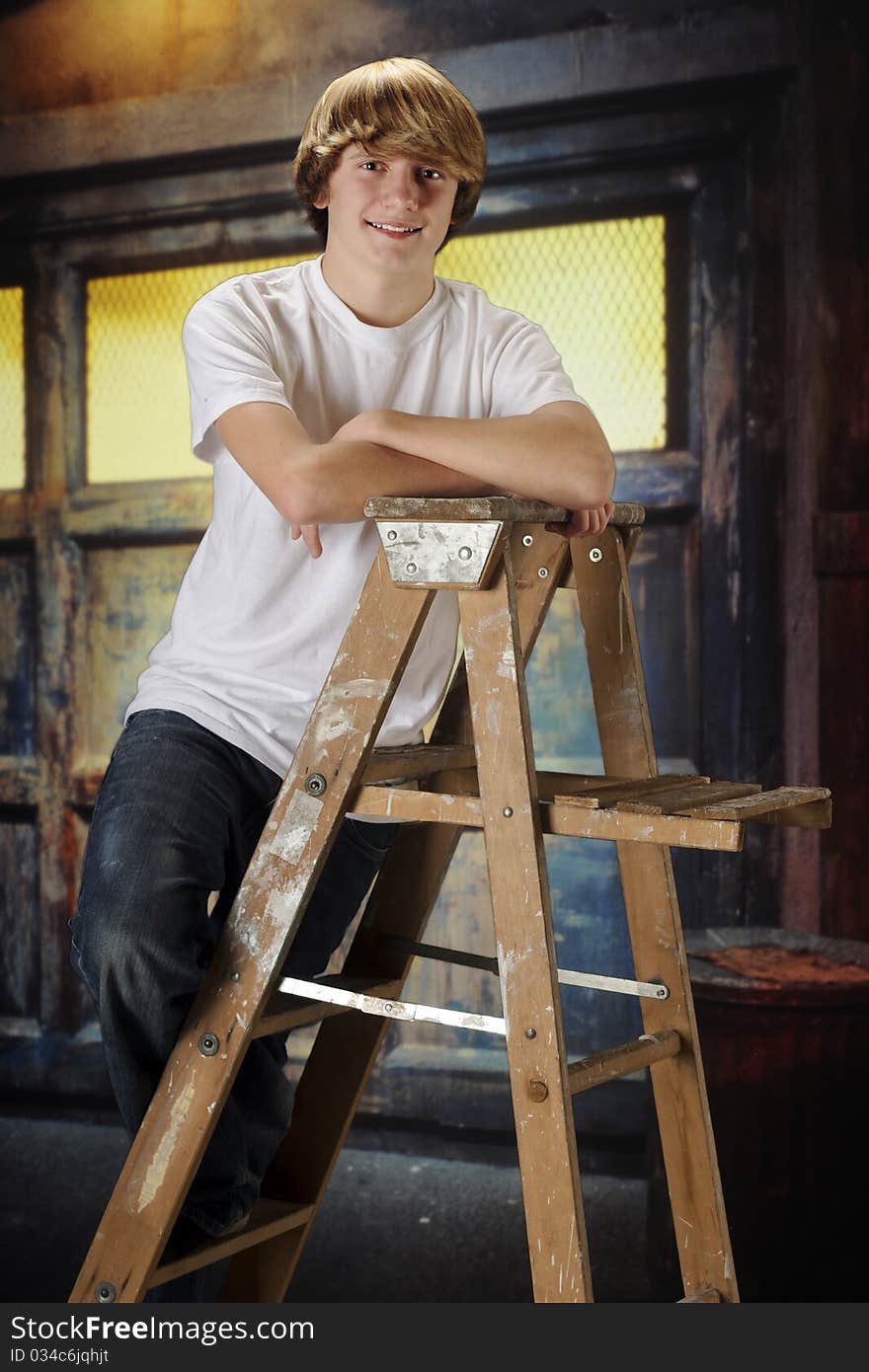 A happy teen boy hangomg on a ladder in a grungy old garage. A happy teen boy hangomg on a ladder in a grungy old garage.